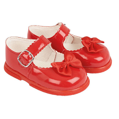 Little girls red, first walker toddler shoes, from our Baypods collection made from faux patent leather with a pretty satin bow on the front. Traditional in style, they have a classic "Mary Jane" shape and buckle fastening strap. Made in England, they have a rubber sole that is soft and flexible, ideal for growing feet. . First walker  Faux patent leather upper Buckle fastening Flexible rubber sole  Made in England