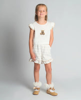 A studio shot of a girl wearing the Beau Kid camel two-piece jersey set featuring a teddy bear graphic top with a ruffled hem and matching shorts.