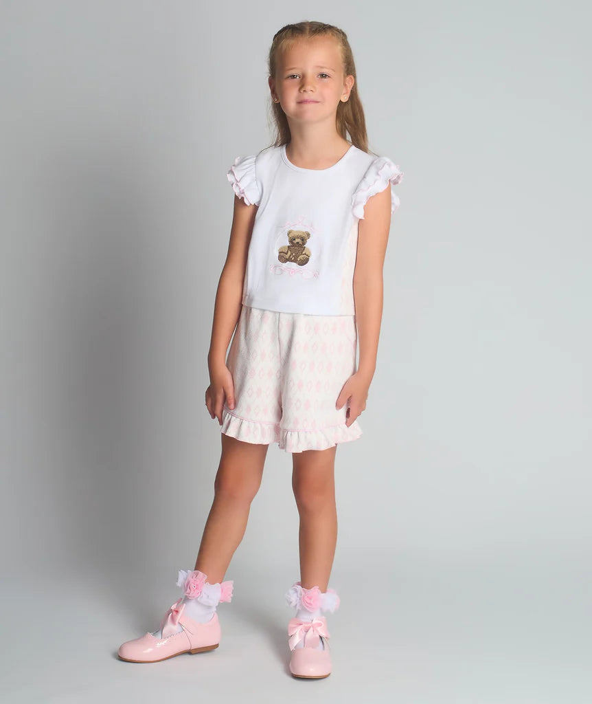 A studio shot of a girl wearing the Beau Kid pink two-piece jersey set featuring a teddy bear graphic top with a ruffled hem and matching shorts.