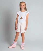 A studio shot of a girl wearing the Beau Kid pink two-piece jersey set featuring a teddy bear graphic top with a ruffled hem and matching shorts.