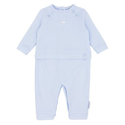 Blues Baby branded boys romper finished in a soft blue colour. This boys romper has a round neck collar with vertical jacquard design down the front and has open feet. Available in sizes 1 month up to 9 month.