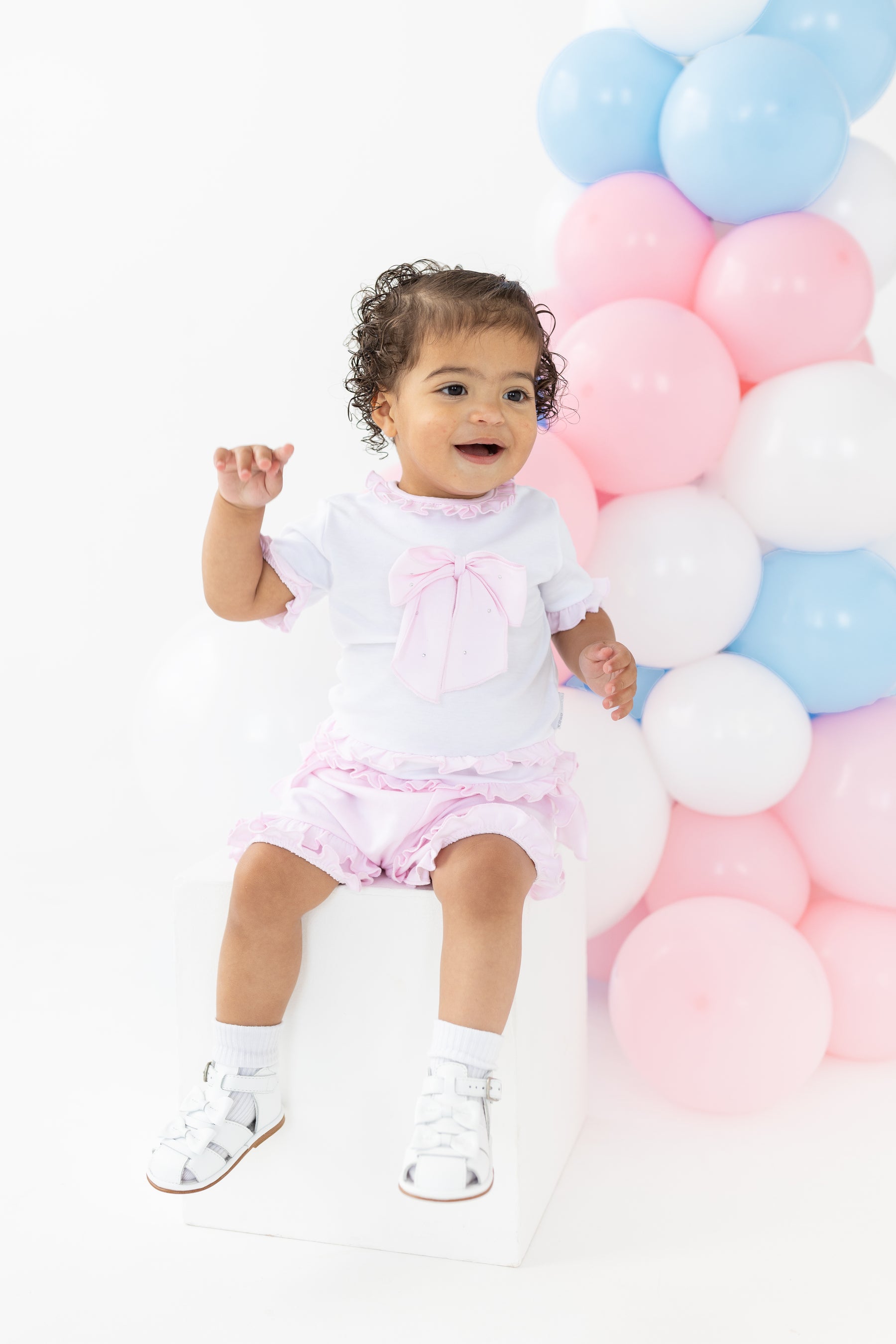 Introduce your little one to style with this adorable two piece set from kids boutique brand Blues Baby. The white t-shirt features a sparkling pink diamanté bow, while the pink frilly shorts add a touch of girly charm. Available in sizes 3 months to 24 months. Perfect for any occasion!