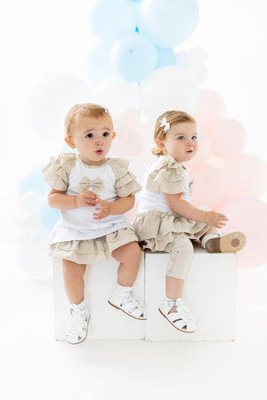 Introduce a beautiful addition to your child's spring and summer collection with Blues Baby's two-piece set. The white top showcases ruffle shoulders in beige and a charming bow accent, complemented by bow-adorned beige bloomer shorts that add a burst of colour. Available in a range of sizes from 3 months to 24 months.