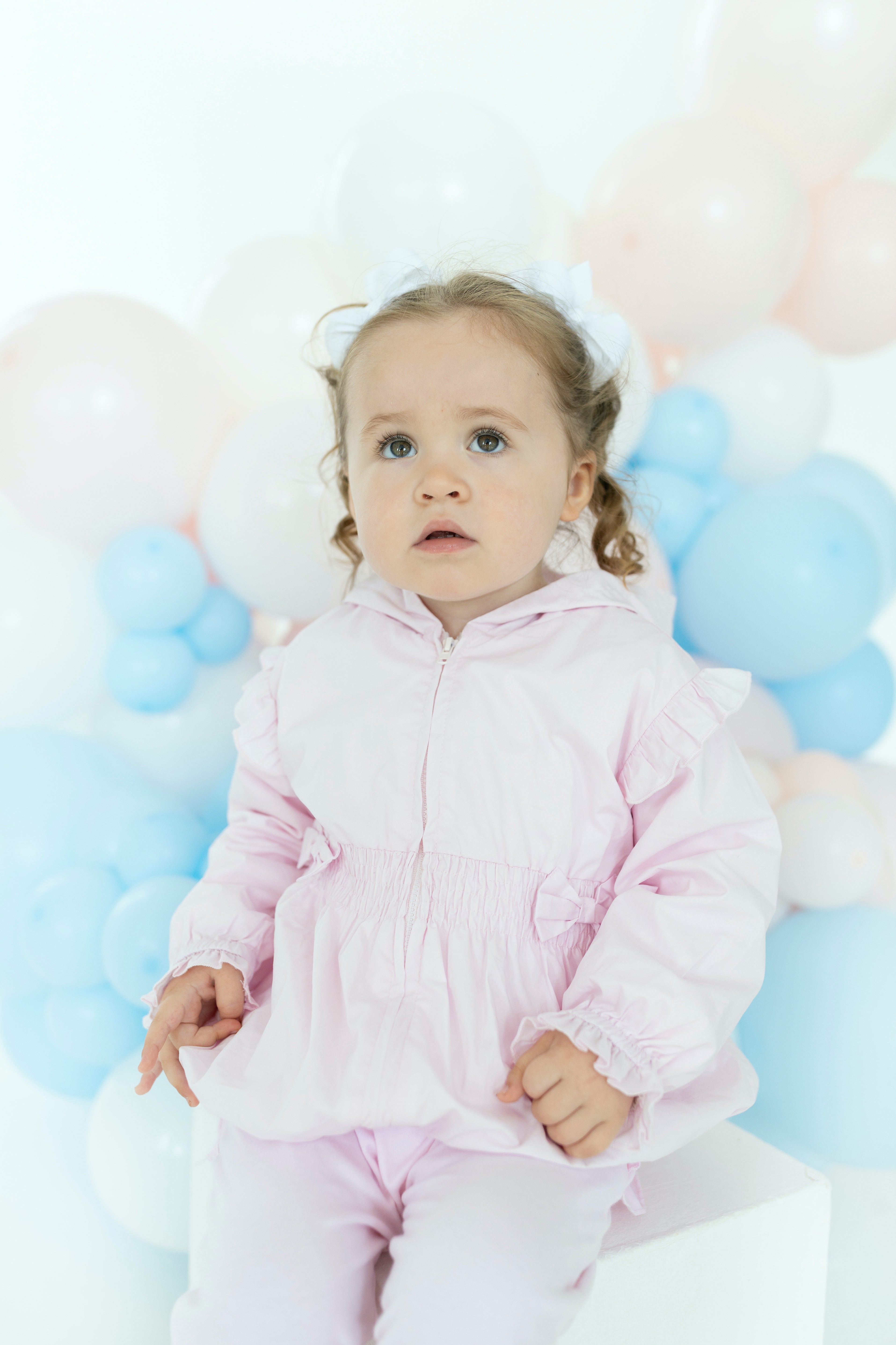 Lifestyle view of a young girl wearing the Blues Baby pink La Rochelle jacket with hood and elasticated frill cuffs
