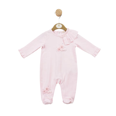 Mintini Baby branded girls all in one babygrow, finished in a soft pink colour. This sleeper has small flower embellishment design to the front and a frill going over the side of the shoulder, which carries on to the back. Push button fastening on the back for easy access. Available in sizes 1 month, 3 month & 6 month.
