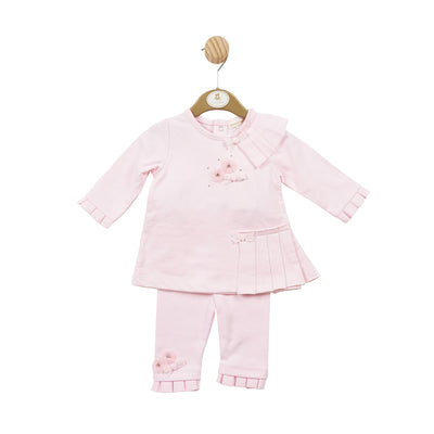 Mintini Baby branded girls two piece tunic and legging set finished in pink colour. This set consists of a long sleeve top which has small flower embellishment to the front, and frill detail around the shoulder and the bottom. Comes with matching leggings which have the same detail. Available in sizes 3 month up to 24 month.