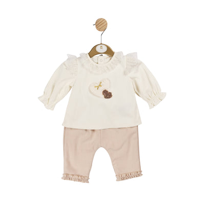 Introducing the perfect autumn/winter matching outfits for sisters, from children's clothing brand Mintini Baby. This two piece set includes a long sleeve ivory top with a delightful heart motif design, frill around the collar and shoulders and beige trousers with a comfortable elasticated waistband and charming ruffled ankle detail. Available in sizes 3 months up to 5 years old. Elevate your little ones' fashion game with our beige, ivory, and gold two piece top and trouser set.