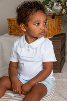 Child wearing a white shirt and light blue shorts sitting on a striped cushion.
