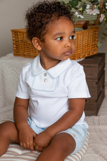 Child wearing a white shirt and light blue shorts sitting on a striped cushion.