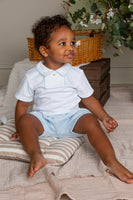 Child wearing a white polo shirt and light blue shorts sitting on a striped cushion.