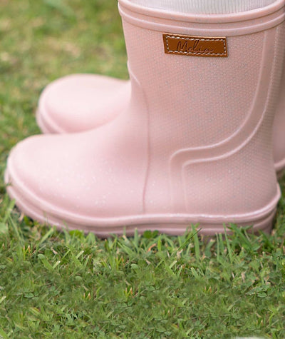 Pink rain boot with a brand label on grass