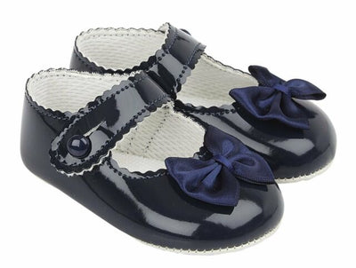 These gorgeous navy pre-walker baby girl shoes, from our Baypods collection, are beautifully made in soft faux patent leather and have pretty satin bows on the toes. Easy to put on, they secure with a button fastening strap. They have a lightly cushioned insole and their flexible soles are just right for developing feet.  . Faux patent leather Lightly cushioned insole  Flexible soles Button fastening strap