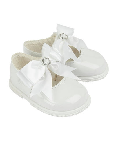 Adorable for little girls taking their first steps, a white pair of first-walker toddler shoes, made from soft patent faux leather. From our Baypods collection, these sweet shoes fasten with a small button strap and have large ribbon bows and diamanté trims. They have a soft rubber sole to provide flexibility and stability.  . Soft patent faux leather uppers Flexible rubber sole Button strap fastening 