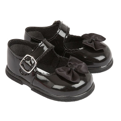 Little girls black, first walker toddler shoes, from our Baypods collection made from faux patent leather with a pretty satin bow on the front. Traditional in style, they have a classic "Mary Jane" shape and buckle fastening strap. Made in England, they have a rubber sole that is soft and flexible, ideal for growing feet. . First walker  Faux patent leather upper Buckle fastening Flexible rubber sole  Made in England