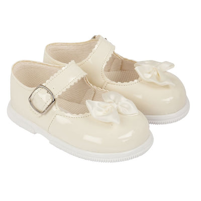 Little girls ivory, first walker toddler shoes, from our Baypods collection made from faux patent leather with a pretty satin bow on the front. Traditional in style, they have a classic "Mary Jane" shape and buckle fastening strap. Made in England, they have a rubber sole that is soft and flexible, ideal for growing feet. . First walker  Faux patent leather upper Buckle fastening Flexible rubber sole  Made in England