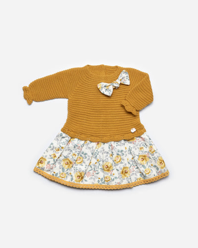 Girls mustard colour knitted dress by Juliana. This long sleeve dress has a floral cotton printed design across the bottom and a matching floral printed bow to the front. Buttons on back opening. Available in sizes 3m up to 4yr.